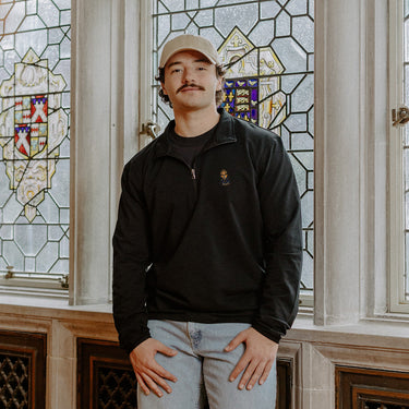 Male model wearing the black Alpha Epsilon Pi Embroidered Luxe Quarter Zip in front of stained glass windows with fraternity crests.