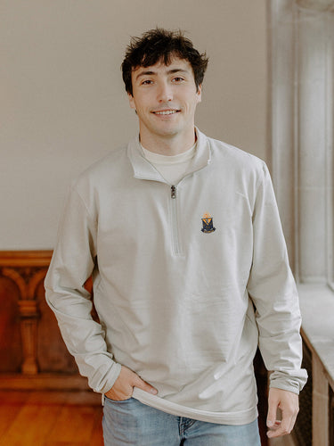 Male model wearing the smoke-colored Alpha Epsilon Pi Embroidered Luxe Quarter Zip with crest embroidery, standing by a window in a formal setting.
