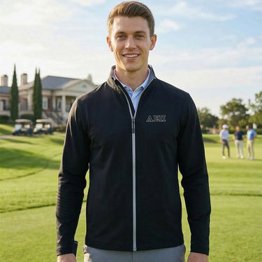Fraternity wearing a black Callaway water-repellent golf jacket standing on a golf course in front of a clubhouse