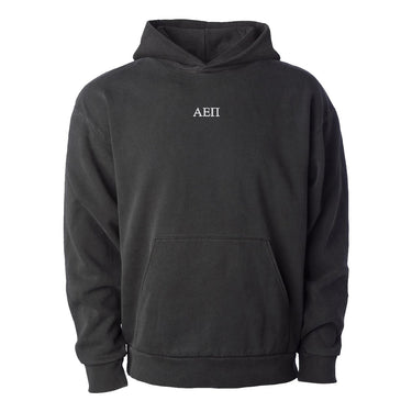 College-aged man wearing the Alpha Epsilon Pi embroidered black hoodie, standing in front of stained glass windows with fraternity-style crest designs.